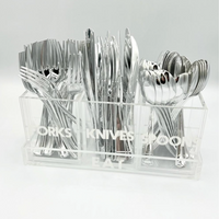 The Eye Candy Let's Eat Silverware Caddy is a clear acrylic tray labeled FORKS, KNIVES, and SPOONS, neatly organizing silverware into compartments—perfect for keeping your dining setup tidy and stylish.