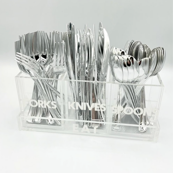 The Eye Candy Let's Eat Silverware Caddy is a clear acrylic tray labeled FORKS, KNIVES, and SPOONS, neatly organizing silverware into compartments—perfect for keeping your dining setup tidy and stylish.