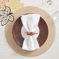 A table setting with a tan placemat, brown plate, and white napkin tied with the Kim Seybert Rope Knot Napkin Ring Set of 4 adds coastal charm. Wine and water glasses plus embroidered leaf details complete the look.