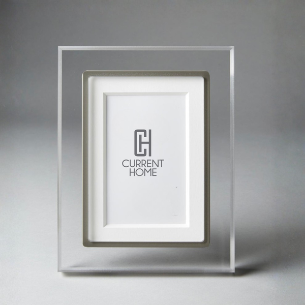 The Prisma Frame Lip - Grey by Bella Moulding is a clear acrylic photo frame with a silver inset and white mat, crafted from archival materials. The frame features the Current Home logo on the white mat.