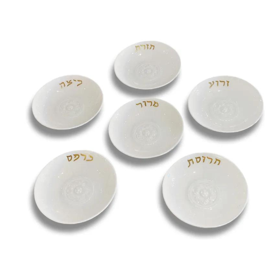 The Bernardaud Louvre Seder Dishes Set of 6 features elegant white plates arranged in a circle, each with a unique Hebrew word in gold script. An ideal heritage gift for Passover Seder, displayed on a plain white background.