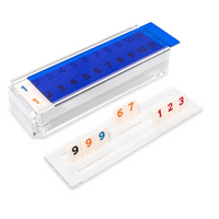 The Luxe Dominoes Rummy Acrylic Game Set features a clear acrylic case with a blue lid and numbered tiles; a tray highlights 9, 9, 6, 7, 1, 2, and 3 in black, orange, and red—perfect for game lovers.
