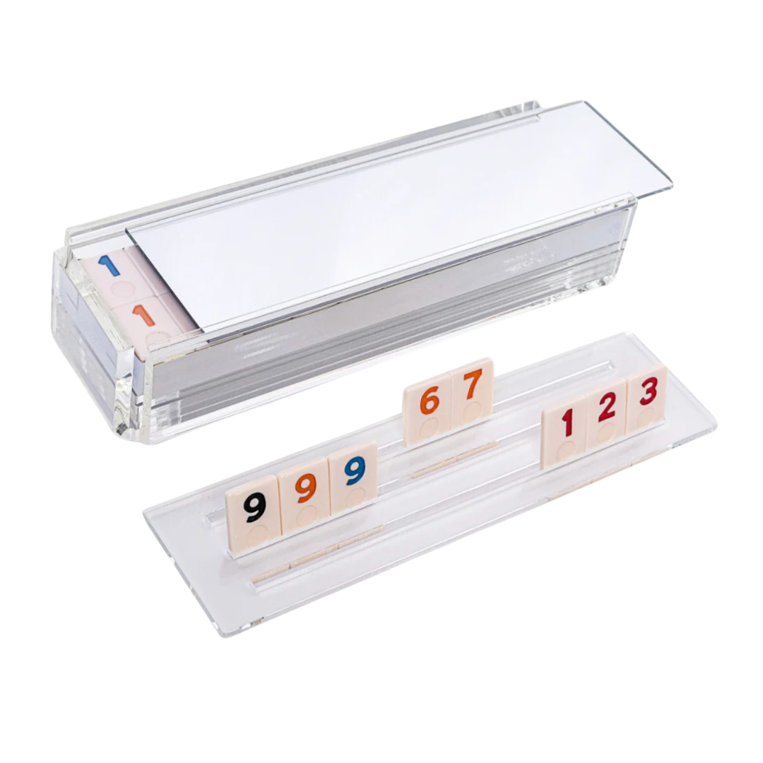 The Luxe Dominoes Rummy Acrylic Game Set features a clear holder with numbered tiles in red, blue, and black—one closed with tiles inside, the other displaying 9, 9, 6, 7, 1, 2, 3—making it an ideal gift.