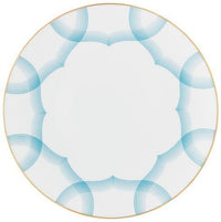 The Aura Dinnerware by Raynaud is a round white plate with a thin gold rim, made in France, featuring overlapping blue curved lines in a symmetrical geometric design near the edges.
