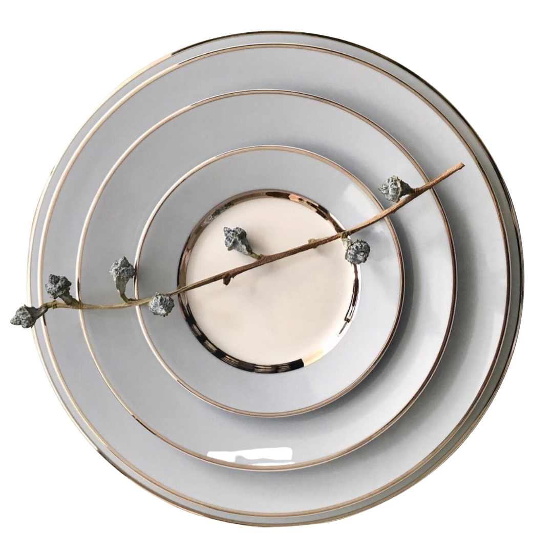 Four stacked Recamier MAK Grey & Platinum plates by Royal Limoges/Bia Cordon Bleu are arranged from largest to smallest, with a delicate branch bearing small buds placed diagonally across this elegant dinnerware set.