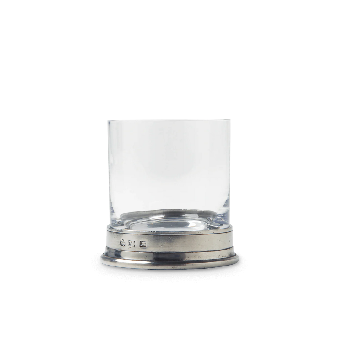A clear, short MATCH Pewter Barware glass of lead-free European crystal with a thick base sits on an engraved Italian pewter coaster by MATCH, set against a plain white background.
