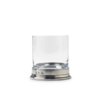 A clear, short MATCH Pewter Barware glass of lead-free European crystal with a thick base sits on an engraved Italian pewter coaster by MATCH, set against a plain white background.