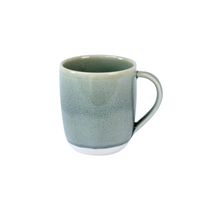 The Maguelone Cachemire Dinnerware by Jars - Rosenthal features a ceramic mug with a light green, slightly textured glaze, curved handle, and white base, presented against a plain white background.