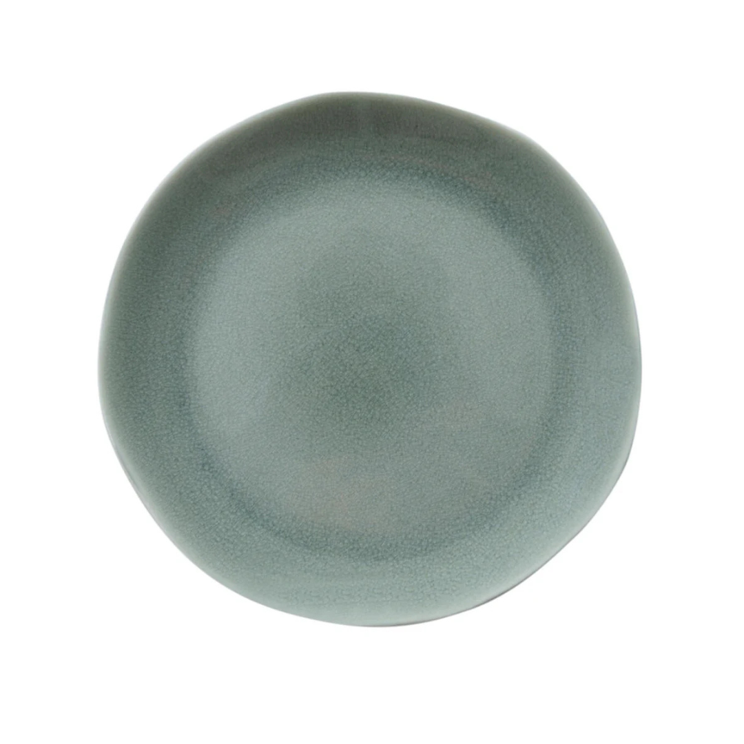 The Maguelone Cachemire Dinnerware by Jars - Rosenthal features a dusty blue, slightly irregular plate with a textured matte finish, displayed top-down on a white background.