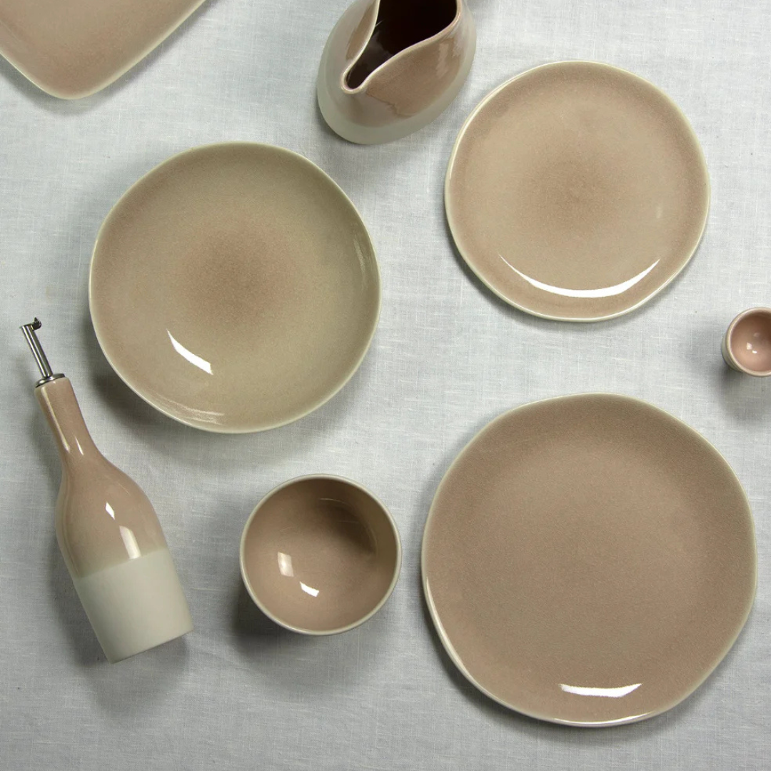 A set of Maguelone Dinnerware Tamaris by Jars - Rosenthal—including plates, bowls, a serving bowl, and oil bottle—is displayed on white linen, featuring smooth semi-gloss and crackled glazes with clean, modern shapes.