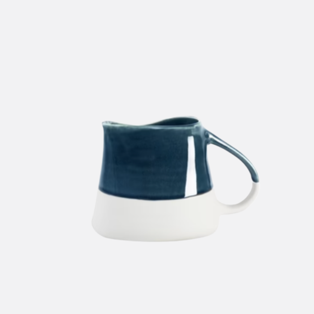 The Maguelone Outremer Dark Blue by Jars - Rosenthal is a small Mediterranean-style ceramic pitcher with a curved handle, glossy dark blue top, and matte white base. Dishwasher safe for easy cleaning. Set against a plain light background.