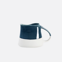 The Maguelone Outremer Dark Blue by Jars - Rosenthal is a small Mediterranean-style ceramic pitcher with a curved handle, glossy dark blue top, and matte white base. Dishwasher safe for easy cleaning. Set against a plain light background.