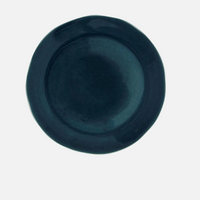 The Maguelone Outremer Dark Blue plate by Jars - Rosenthal is a round, dark blue ceramic piece with a subtly wavy edge, part of their Mediterranean-inspired collection, displayed on a plain white background.