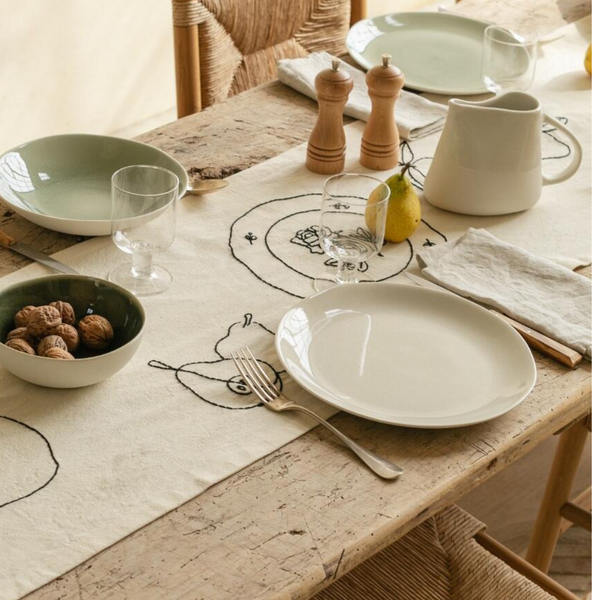 A rustic table is set with Maguelone Dinnerware Quartz by Jars - Rosenthal, a pear sketch table runner, plates, glasses, walnuts, and a pitcher.