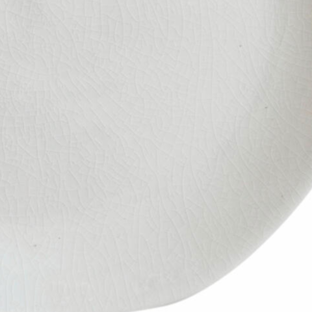 Close-up of the Maguelone Dinnerware Quartz plate by Jars - Rosenthal, featuring a white ceramic surface with a subtle crackle texture and an elegantly curved edge that highlights its artisanal craftsmanship.
