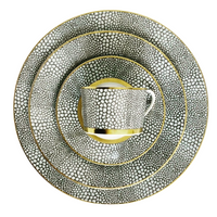 The Makassar Gold Dinnerware set by Royal Limoges features a cup, saucer, and three plates with a black and white pebble pattern and gold trim, expertly handmade in France from fine Limoges porcelain.