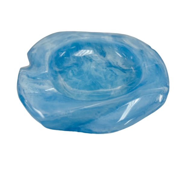 The Lily Juliet Malibu Resin Dish is a translucent blue ashtray with a marbled pattern, rounded shape, and cigarette groove. Crafted from durable resin, this unique design is shown on a white background.