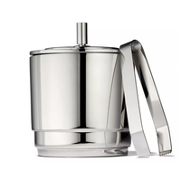 The Georg Jensen Manhattan Ice Bucket & Tong Set features a smooth, shiny finish and modern design inspired by Art Deco elegance, complete with a lid and matching tongs, set against a white background.