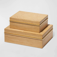 Two Marcello Box Oak by Aerin, crafted from European oak with gold hinges, are stacked atop each other. Their light wood finish and sleek lines make them elegant decorative desk organizers against a plain white background.