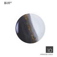 A round porcelain Marie Daâge Horizon Gold Dinnerware plate features a black, gray, and white gradient with a hand-painted gold accent on the transition. The Marie Daâge logo is top left; "Horizon Gold" appears at the bottom right.