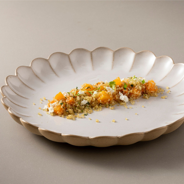 A scalloped Marrakesh Dinnerware White plate by Casafina/Costa Nova features a small portion of quinoa salad—orange squash, white cheese, and herbs—arranged in a neat line on a neutral background.