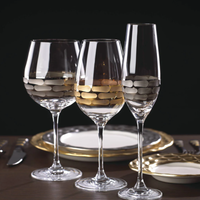 Two elegant Truro Red Wine Platinum glasses by Michael Wainwright, with matching gold-accented plates and cutlery, are set on a table against a dark background.