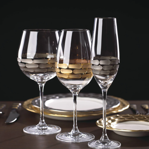 Two elegant Truro Red Wine Platinum glasses by Michael Wainwright, with matching gold-accented plates and cutlery, are set on a table against a dark background.