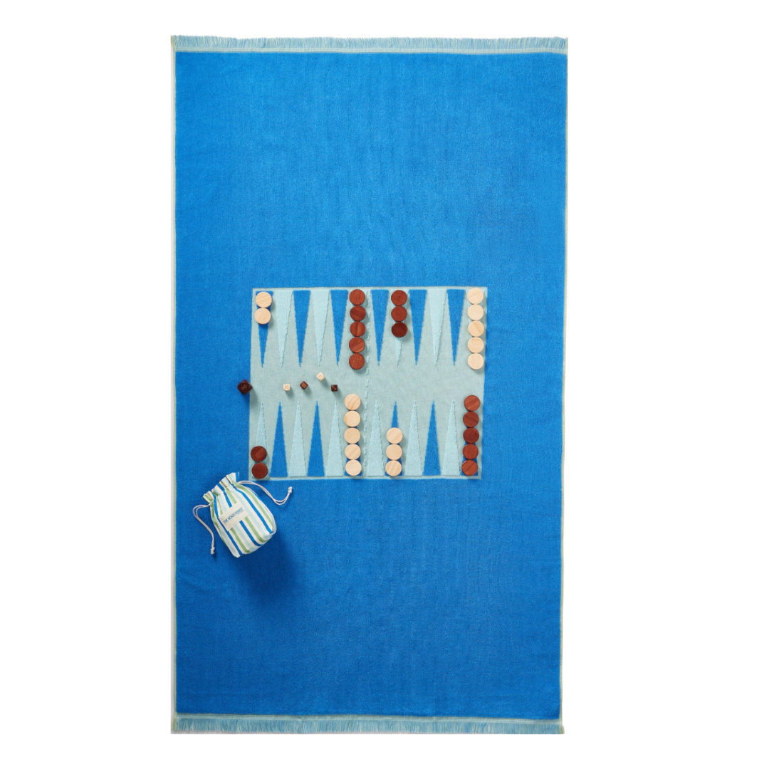 The G. McGee Beach Montauk Backgammon towel features a bright blue terrycloth with a central board design, arranged game pieces, and a striped pouch for storage.