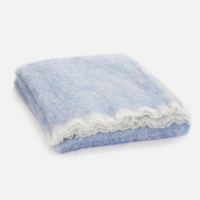 The Cushendale Mooneen Mohair Throw, featuring a folded blue and white design with delicate fringe, is displayed against a white background.