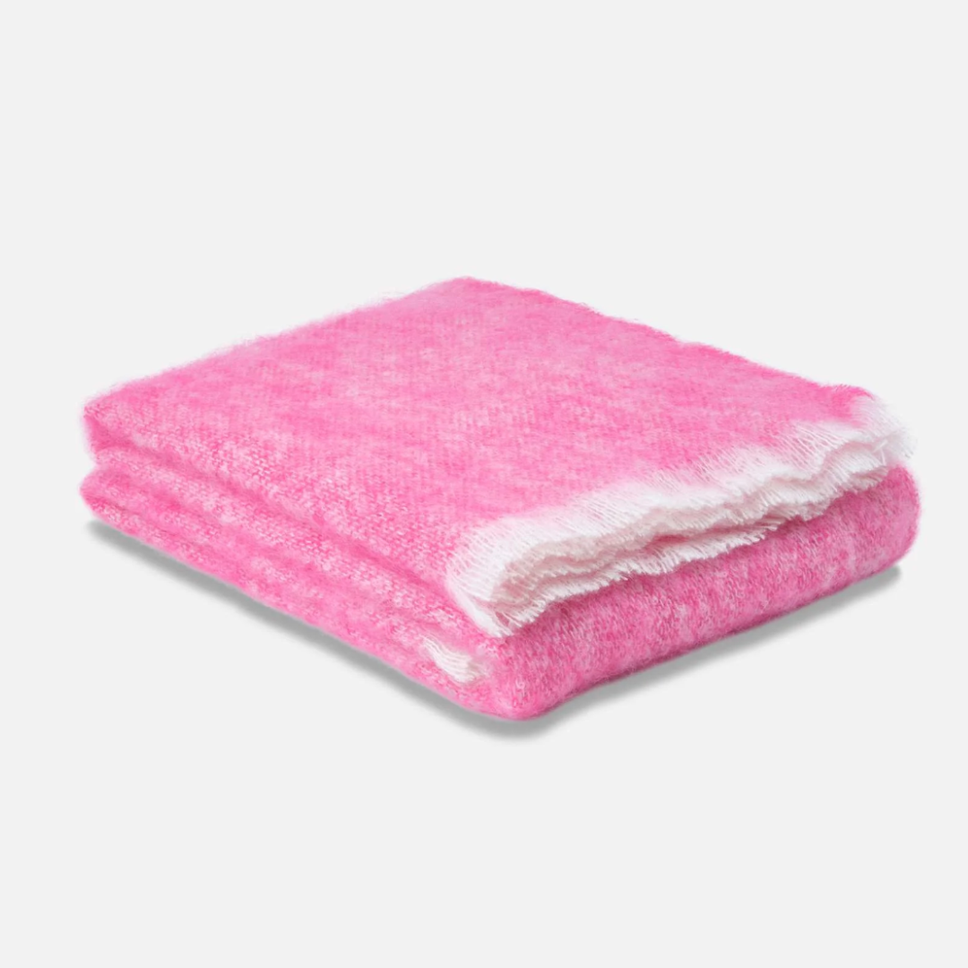 The Cushendale Mooneen Mohair Throw, a fluffy pink luxury blanket with a white border, is folded on a light gray surface against a plain white background.