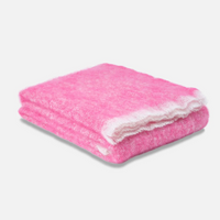The Cushendale Mooneen Mohair Throw, a fluffy pink luxury blanket with a white border, is folded on a light gray surface against a plain white background.
