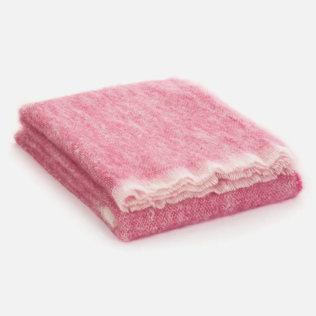 The Cushendale Mooneen Mohair Throw, exceptionally soft and fluffy in a pink shade with white edges, is shown folded on a plain white surface.