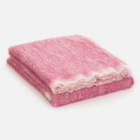 The Cushendale Mooneen Mohair Throw, exceptionally soft and fluffy in a pink shade with white edges, is shown folded on a plain white surface.