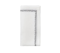 The Kim Seybert Filament Napkin White & Gunmetal Set of 4 features neatly folded white linen napkins with an elegant gunmetal stitched border, displayed against a plain white background.
