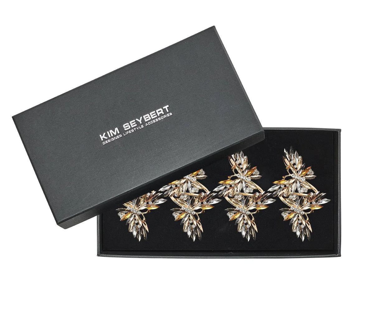 A black Kim Seybert box, partially open, holds the Butterflies Napkin Ring Set of 4—ornate napkin rings with leaf shapes accented by rose gold and rhinestones, with the decorative accessories visible inside.