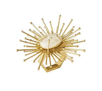 The Flare Napkin Ring Gold Set of 4 by Kim Seybert features a central oval stone with gold rods and spheres radiating out, evoking a sunburst. Handmade, this set adds a brilliant accent to any table setting.