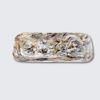 The Nashi Home Swirl Colored Resin Rectangle Platter is shatter-resistant, with rounded edges and a marbled pattern in brown, white, gray, and gold on a plain light gray background.