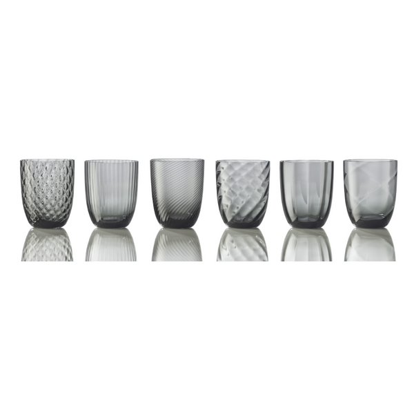 The Nason Moretti Idra Mixed Pattern Glass Set of 6 includes uniquely textured gray tumblers, inspired by Murano glass and made in Italy. Displayed on a reflective white surface.