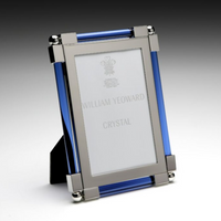 The New Classic Frame Blue by William Yeoward features a rectangular design with nickel-plated silver corners and blue cylindrical side accents, standing upright on a surface. The brand name appears subtly on the insert.