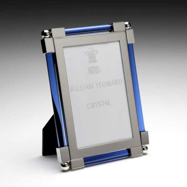 The New Classic Frame Blue by William Yeoward features a rectangular design with nickel-plated silver corners and blue cylindrical side accents, standing upright on a surface. The brand name appears subtly on the insert.