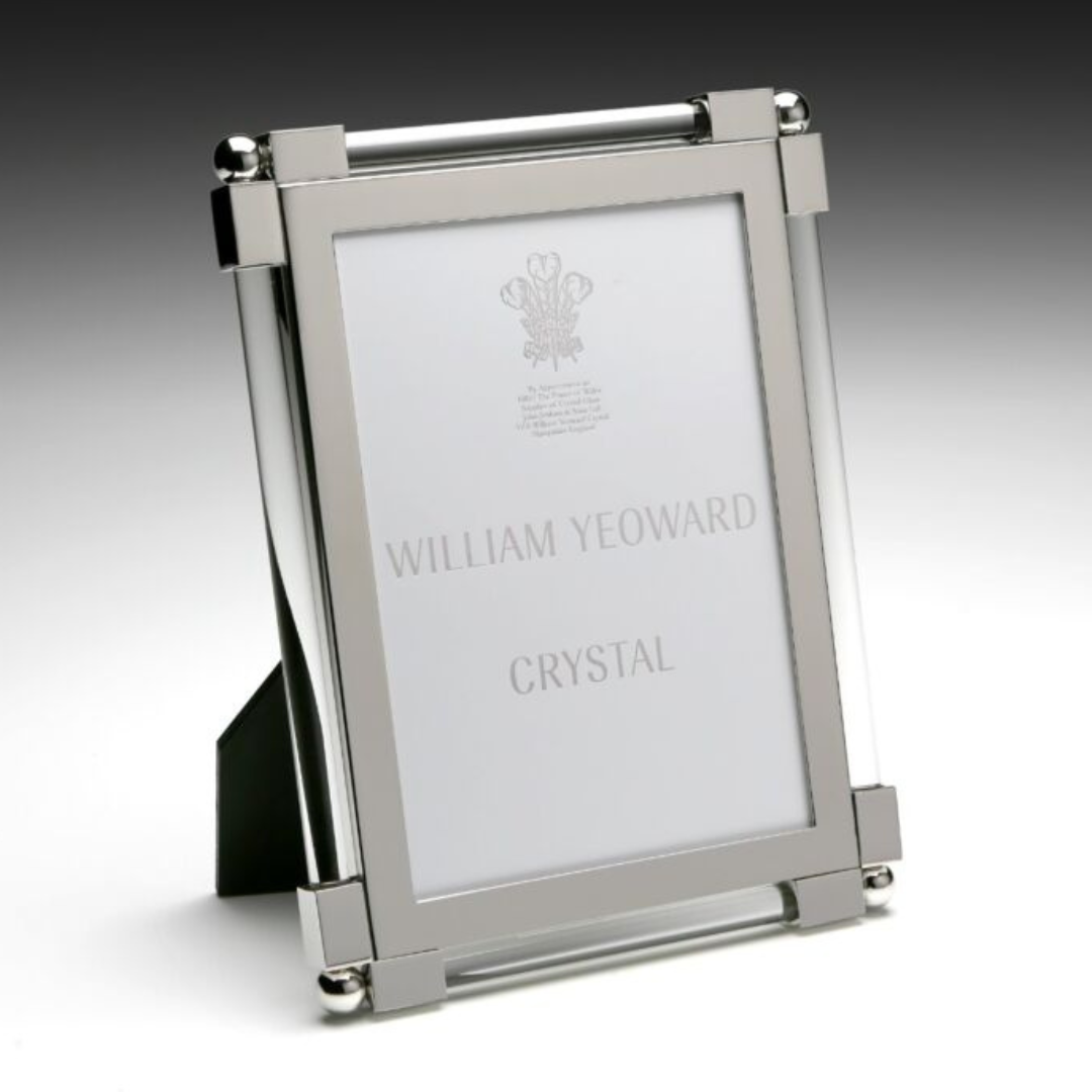 A sleek, clear New Classic Frame by William Yeoward stands upright on a black support. Inside, a placeholder reads "WILLIAM YEOWARD" with a faint crest above it, adding timeless elegance.