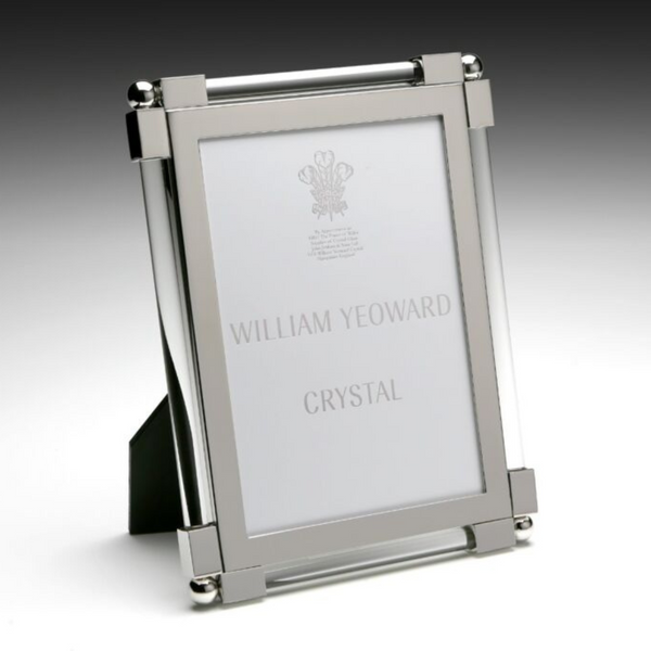 A sleek, clear New Classic Frame by William Yeoward stands upright on a black support. Inside, a placeholder reads "WILLIAM YEOWARD" with a faint crest above it, adding timeless elegance.