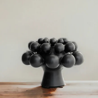 A black abstract tree sculpture sits on a wooden surface next to the KleinReid Nimbus Dome Vase Onyx, with both displayed against a plain, light-colored background.