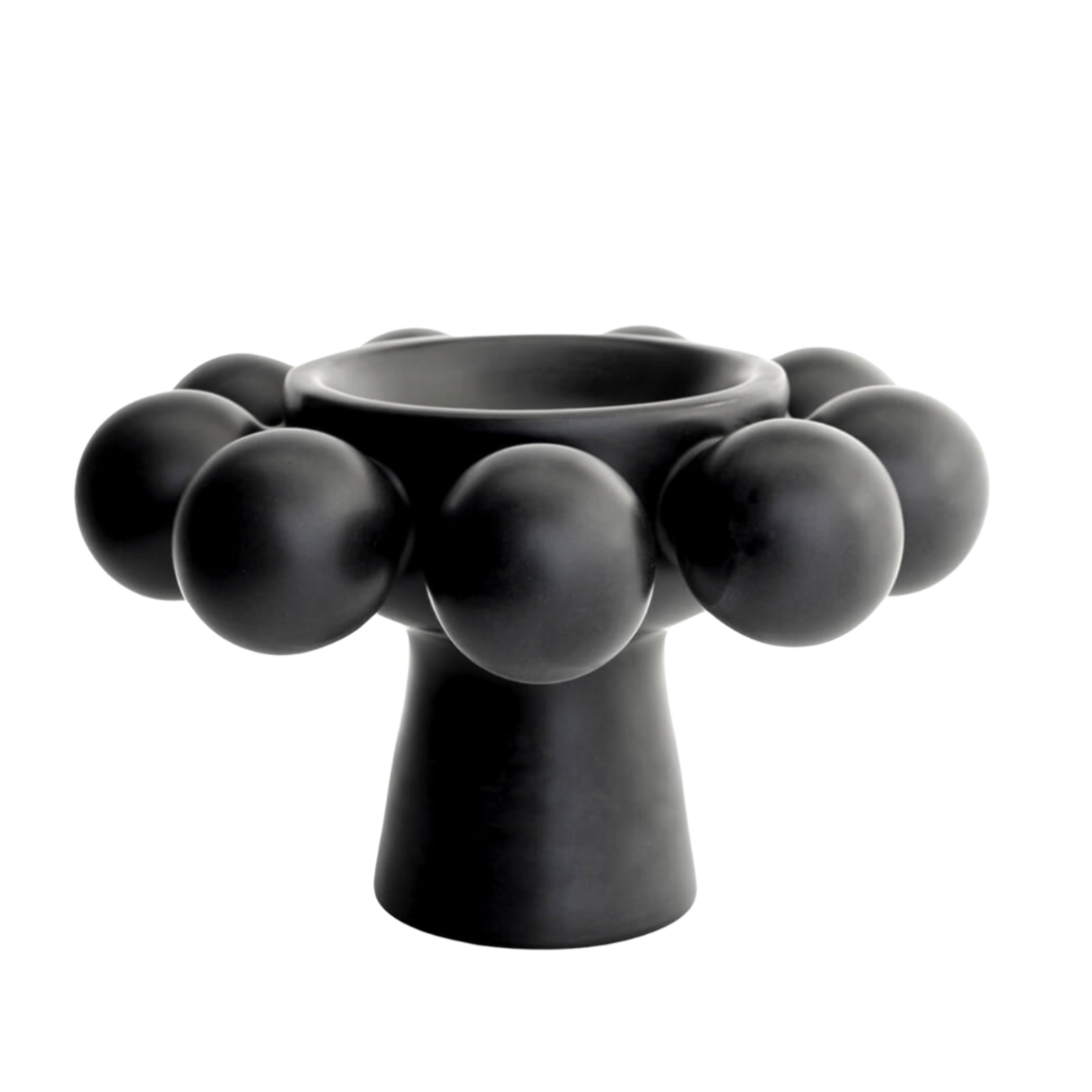 The Nimbus Footed Bowl Onyx by KleinReid, a black porcelain piece with a wide bowl, narrow stem, and spherical accents on its rim, stands on a white background.
