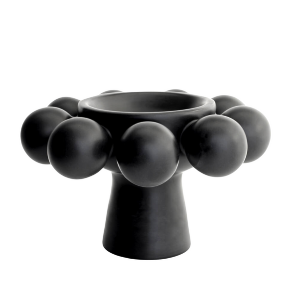 The Nimbus Footed Bowl Onyx by KleinReid, a black porcelain piece with a wide bowl, narrow stem, and spherical accents on its rim, stands on a white background.