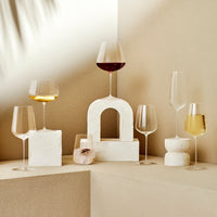 A pair of Nude Glassware’s Stem Zero Vertigo Water Glasses, crafted from lead-free crystal, is displayed on geometric white stone pedestals against a beige background with soft shadows.