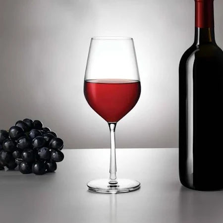 A glass of red wine, a dark wine bottle, and black grapes rest on a table against a gray backdrop—perfect for highlighting your Nude Glassware Climats All Purpose Wine & Water Glass Set of 2.