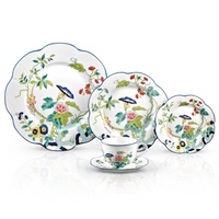 The Royal Limoges Nymphea Paradis Bleu set includes four plates and a teacup, each featuring colorful floral and bird motifs on white porcelain with scalloped blue-rimmed edges.