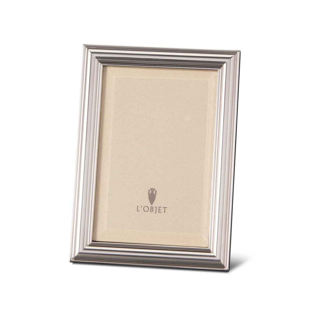 The Oscar Frame Platinum by L'Objet is a silver rectangular frame with a ridged border and sleek angular design, standing upright to display a blank insert featuring the L'Objet logo at the center.
