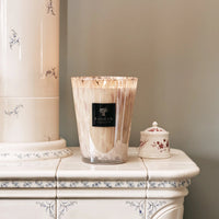 A Baobab Candle Pearls White sits on a white ceramic stove with blue floral designs, next to a small white jar with a red floral pattern, set against a light beige wall.